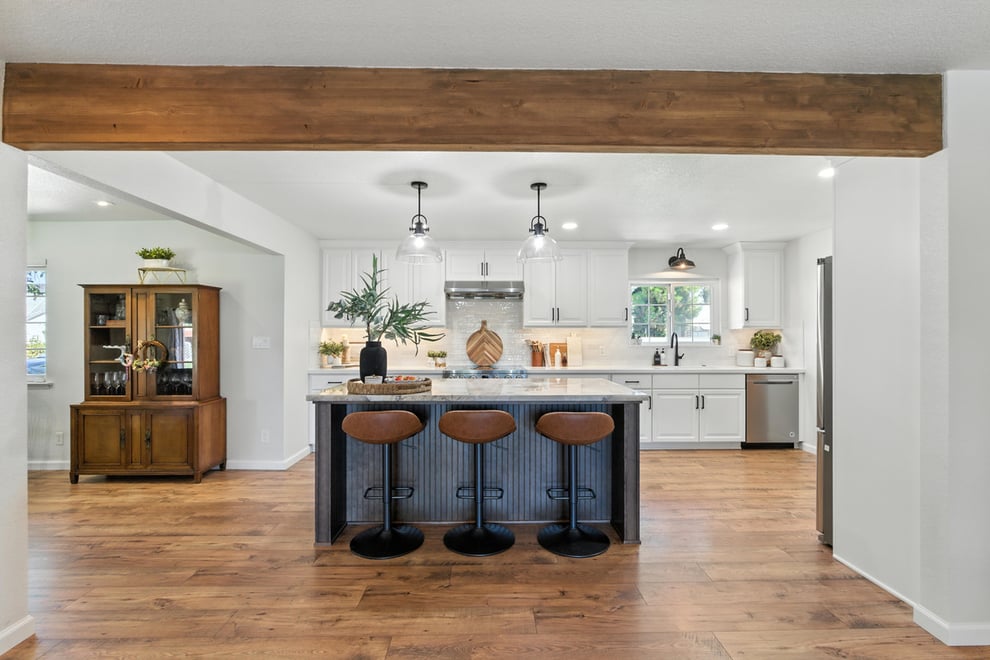 Kitchen island in Clovis, CA with seating and open kitchen beyond, seen from adjacent living space and framed by large architectural beam