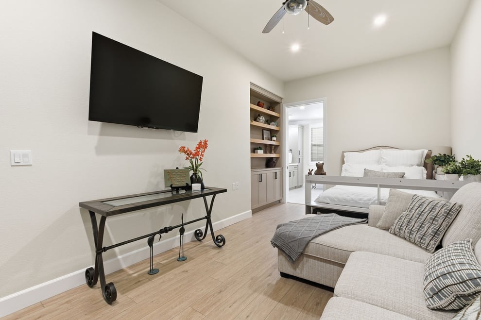 Sitting room with wall-mounted TV and shelving beside a bright bedroom entrance in Fresno