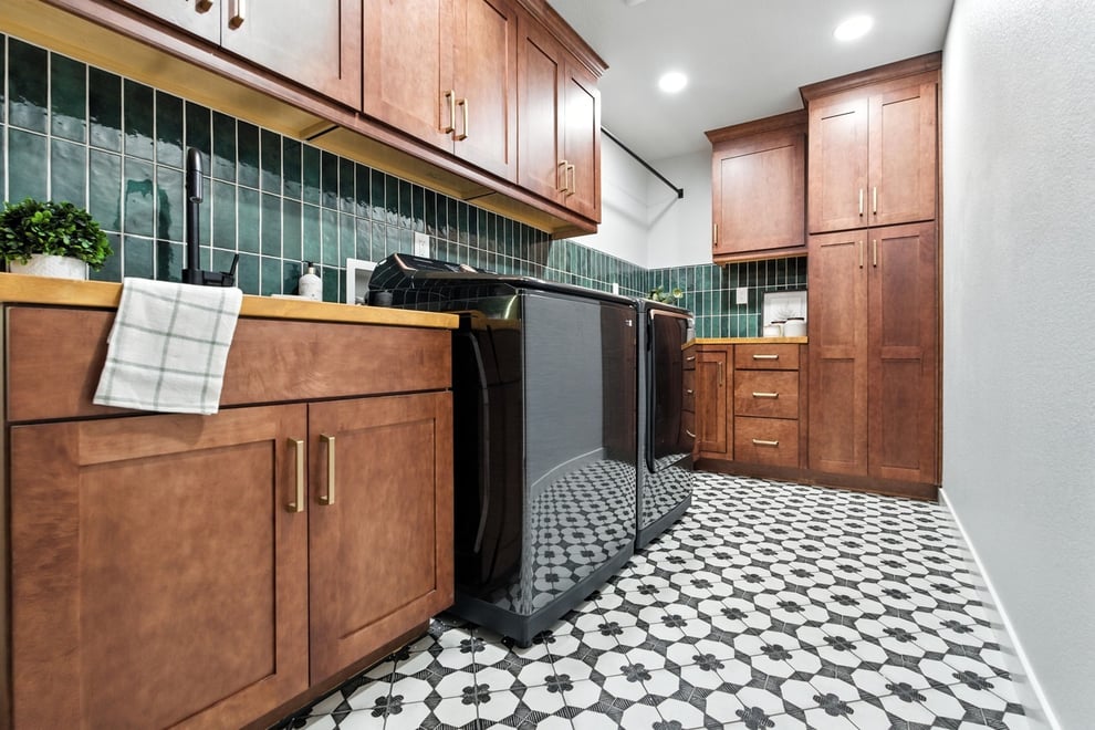 Laundry room with wood cabinets, green tile backsplash, black appliances, and patterned floor in Fresno CA
