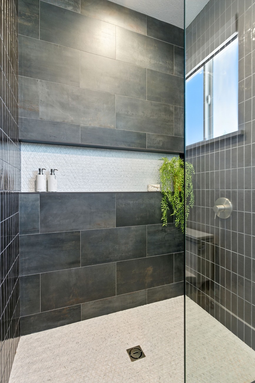 Fresno shower with dark tile, white textured niche, and greenery beside a window