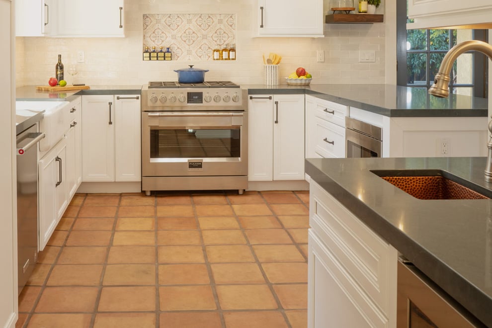 Bright kitchen in Fresno, CA featuring terracotta tile flooring, white cabinetry, copper range hood, and a spacious island with barstools-1
