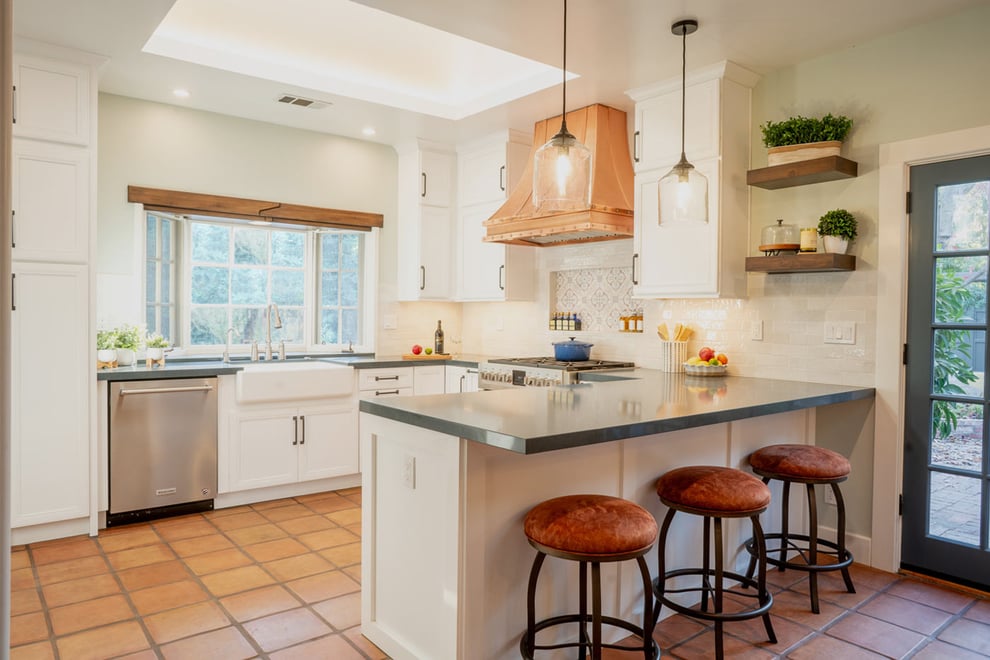 Contemporary Spanish kitchen in Fresno, CA with terracotta tile floors, white cabinets, copper range hood, and large island with barstools