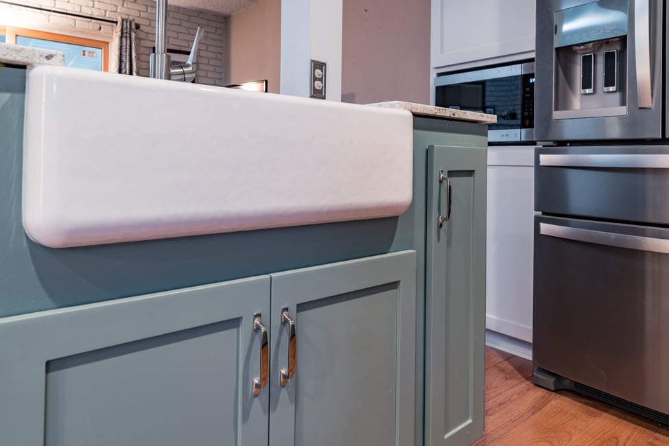farmhouse kitchen sink above light blue shaker cabinets with silver pulls
