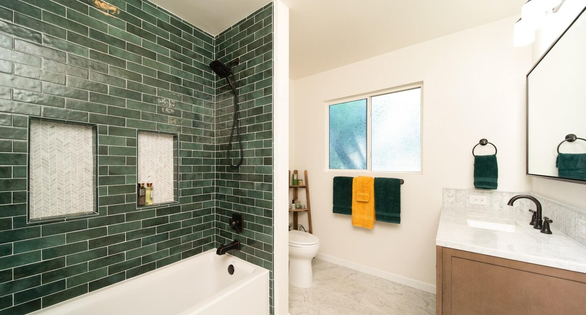 modern minimal bathroom tub with green tiling and white chevron tiling shower niche and concealed commode in fresno